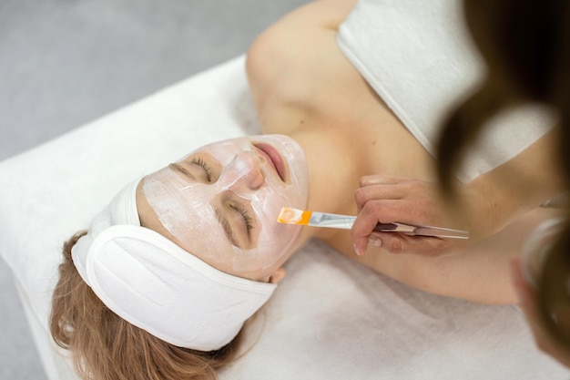 Cosmetologista coloca uma máscara no rosto com um pincel para uma jovem