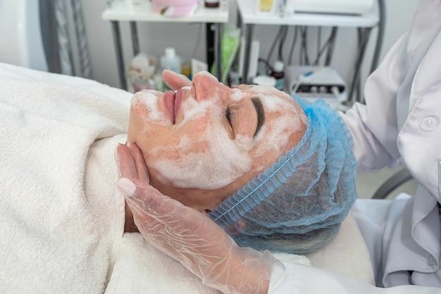 Cosmetologista com pincel aplica uma máscara cosmética no rosto de um cliente em um salão de beleza