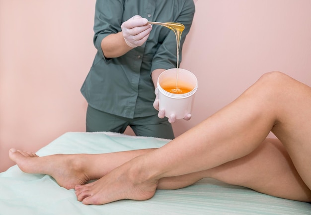 Foto cosmetologista e cliente no processo de depilação de pernas com açúcar líquido em um spa centerleg sugar