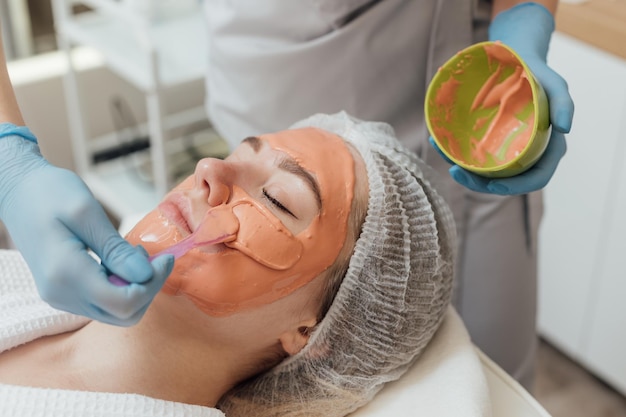 Cosmetologista facial de máscara de geléia cosmética aplica máscara de alginato com espátula no rosto