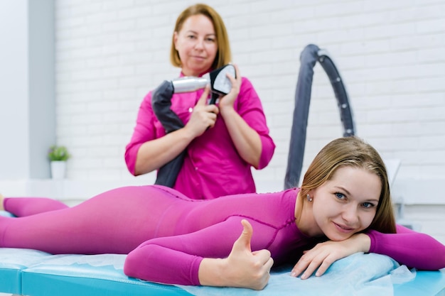 Cosmetologista fazendo massagem anticelulite LPG para mulher de terno gpl rosa Mulher de beleza sorrindo e levantando o dedo