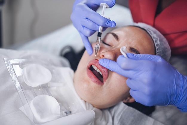 Cosmetologista fazendo um doloroso procedimento de aumento dos lábios com ácido hialurônico o esteticista perfurando os lábios com agulha mulher sofrendo injeção subcutânea para aumentar a forma dos lábis com enchimento dérmico