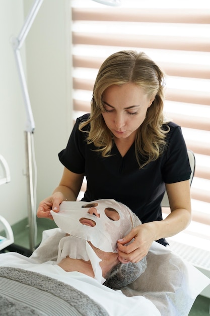 Cosmetologista feminina aplicando máscara de folha no rosto de clientes na clínica de beleza