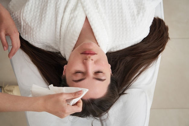 Cosmetologista limpando o rosto de um paciente com algodão em salão de beleza e spa se preparando para