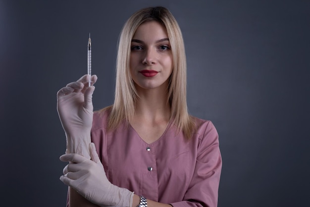 Cosmetologista loira segura uma seringa na mão em um fundo cinza