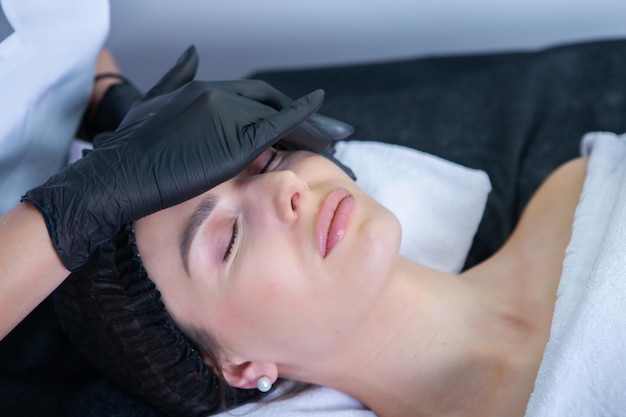 Cosmetologista profissional a fazer massagem facial a uma mulher num salão de spa.
