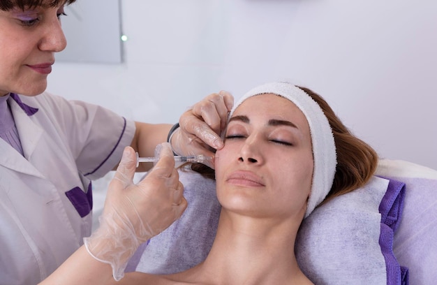 Cosmetologista realiza injeções de enchimento antirrugas rejuvenescedoras com enchimento de ácido hialurônico no rosto de uma mulher Cosmetologia estética feminina em um salão de beleza