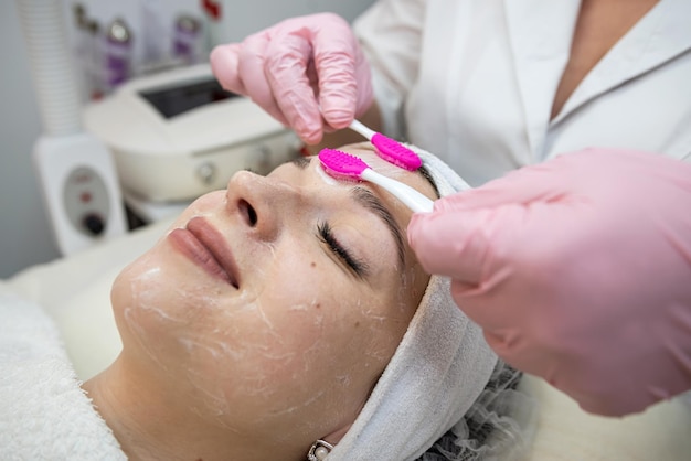 cosmetologista usa uma escova especial aplica creme para o rosto de sua cliente mulher no salão de spa Spa tratamento de beleza conceito de cuidados com a pele