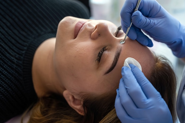 Cosmetologista usando colher de instrumento mecânico para remoção e limpeza de cravos no rosto de uma paciente em um salão de beleza