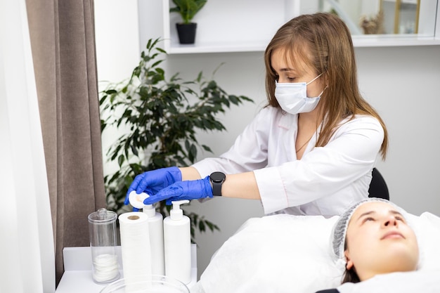 Cosmetologista usando luvas de borracha e uma máscara está limpando uma almofada de algodão em creme ou gel para continuar a limpar o rosto dos clientes dos restos de uma máscara cosmética