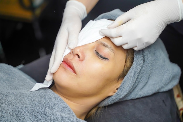 Cosmetologistas de close-up limpando o rosto de uma mulher de beleza asiática antes de fazer spa facial e máscara facial