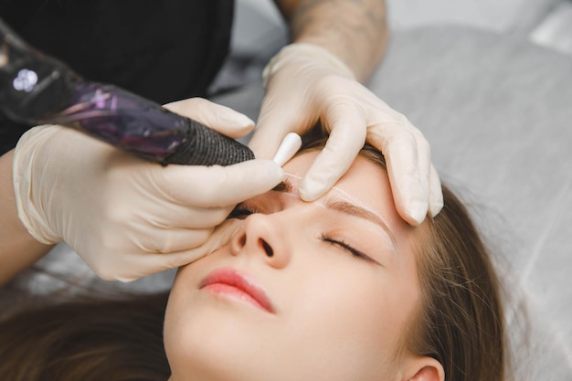 Un cosmetólogo aplica maquillaje permanente a las cejas tatuaje de cejas permanente de cejas