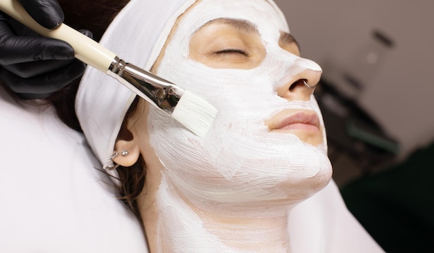 Cosmetólogo aplica máscara facial a la clienta femenina hace procedimientos en un spa o salón