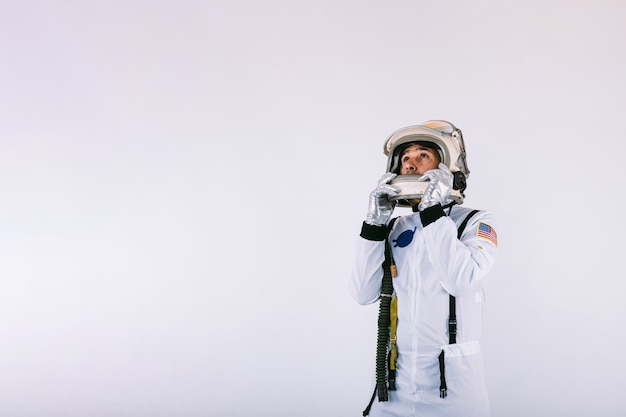 Cosmonauta masculino em traje espacial e capacete segurando um capacete com as mãos no fundo branco