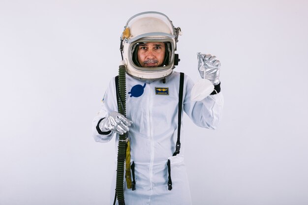 Cosmonauta masculino en traje espacial y casco, sosteniendo una máscara FPP2, sobre fondo blanco. Covid-19 y concepto de virus
