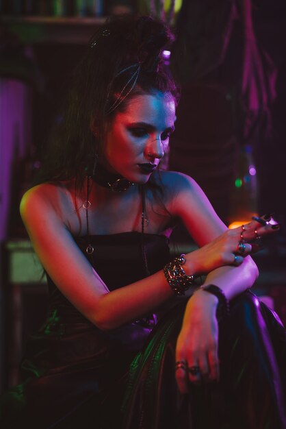 Cosplay de Cyberpunk. Una chica al estilo steampunk del futuro fuma un cigarrillo en un estilo post-apocalíptico. Garaje con luz de neón