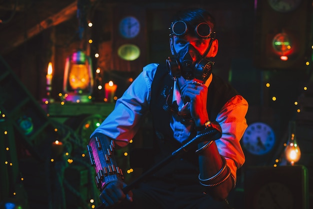 Cosplay cyberpunk post-apocalipsis. Un ingeniero de sexo masculino con gafas y una máscara de gas en un taller con una luz de neón