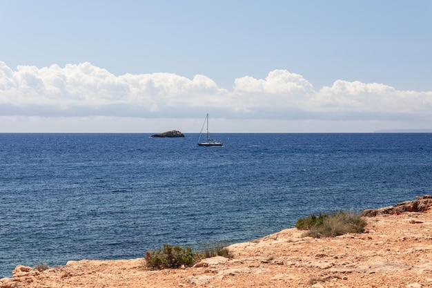 Costa de arenito rochoso com ondulações de vegetação esparsa no iate à vela marítima com velas recolhidas Ibiza