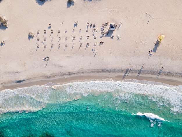 Costa de praia de areia branca com pessoas tomando sol e surfando vista aérea superior