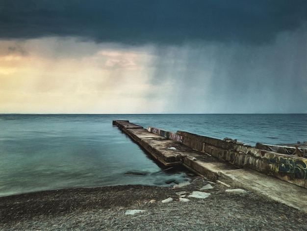 Costa do mar com um longo cais e chuva no mar ilustração