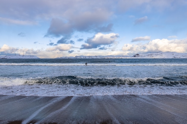 Costa do mar de Barents. Os surfistas surfam nas ondas geladas