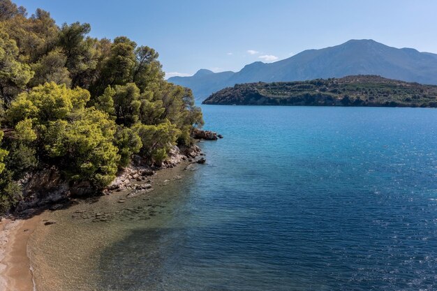 Costa do Mediterrâneo com rochas de praia cobertas de árvores densas e montanhas em uma névoa azul na Grécia