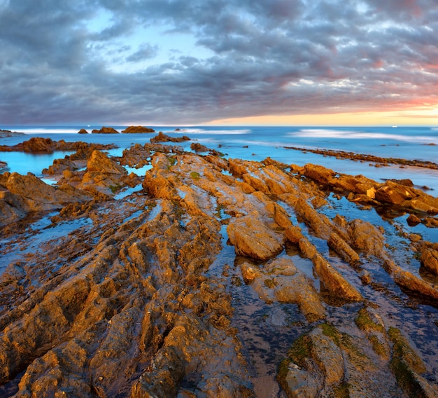 Costa do oceano crepuscular com rocha estratiforme com nervuras