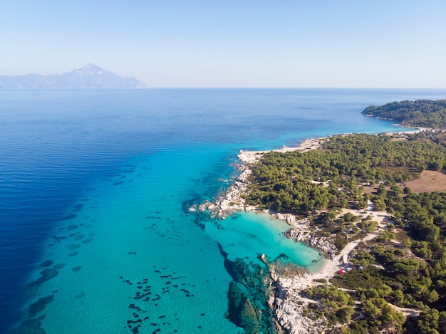 Costa del mar Egeo con agua azul transparente, vegetación alrededor, rocas, arbustos y árboles, vista desde el drone, montaña Grecia