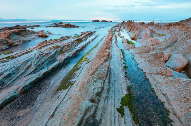 Costa del océano crepuscular con formaciones rocosas estratiformes acanaladas. (Océano Atlántico, España).