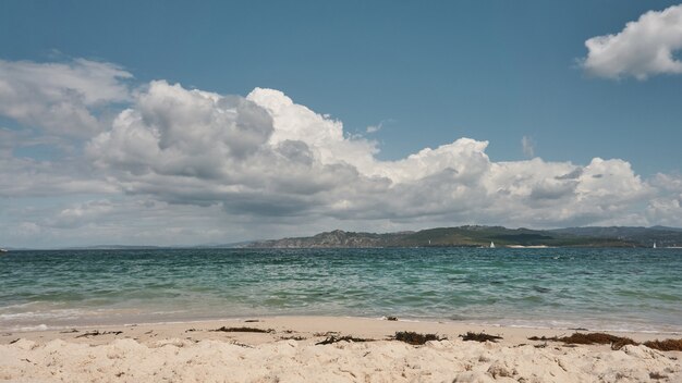 Foto costa de playa con arena blanca, aguas cristalinas y nubes en el cielo.