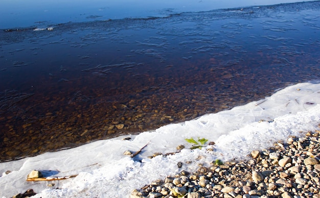 Costa rochosa com água gelada Gelo e neve na costa do lago