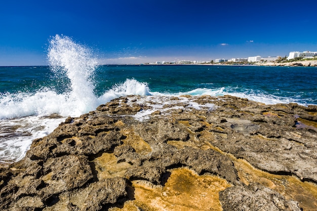 Costa rocosa, agua de mar turquesa clara y las olas rompen con salpicaduras en las rocas, cielo azul. ayia-napa, chipre.