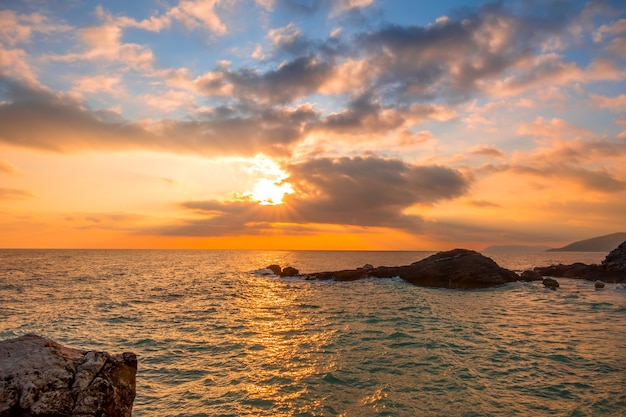 Costa rocosa. Muchas nubes rosadas en el cielo y los rayos del sol.