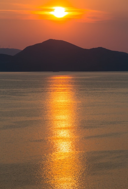 Costa de verano por la noche con puesta de sol rosa-amarilla, pista de sol e isla en el horizonte