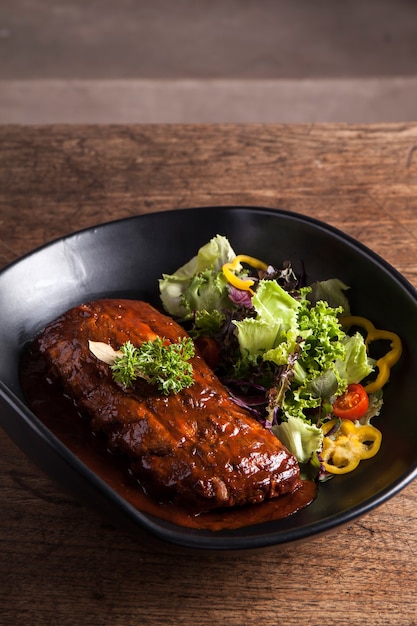 Costela com molho e salada fresca em prato preto