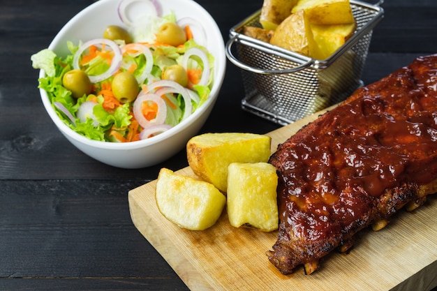 Costela de churrasco com batata e salada em uma tábua