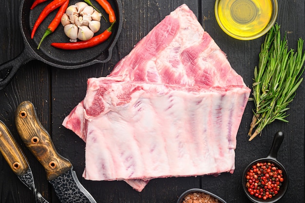 Costela de porco com conjunto de ingredientes, com mel, com faca de churrasco e garfo de carne, na mesa de madeira preta, vista de cima plana lay