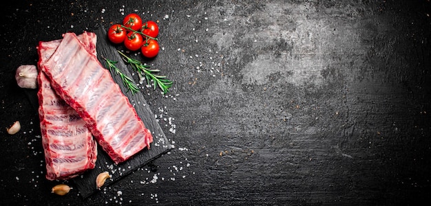 Costelas cruas em um tabuleiro de pedra com tomates e pedaços de sal