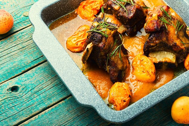 Costelas de carne cozidas em damascos. Carne de vitela com molho de frutas em fundo de madeira rústico