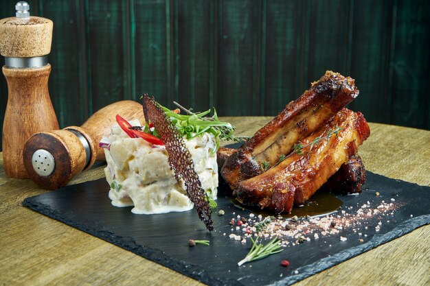 Costelas de porco grelhadas suculentas em molho de mel e cerveja em uma bandeja preta com um prato de batatas cozidas. food pub. lanche de cerveja. fechar-se. foco seletivo. copie o espaço