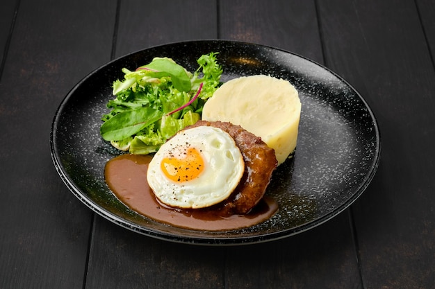 Costeleta de carne com ovo frito, purê de batata e salada fresca em um prato