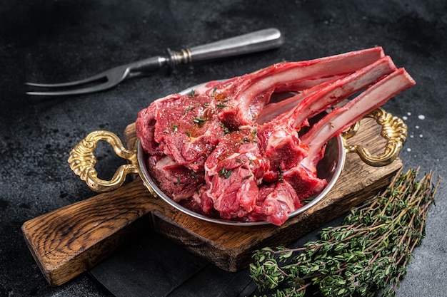 Costeleta de carne crua de bife de carneiro de cordeiro em uma frigideira com ervas Fundo preto Vista superior