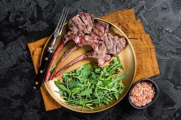 Costeleta de cordeiro grelhada para churrasco ou bife de costeleta de carneiro com salada de rúcula em um prato Fundo preto Vista superior