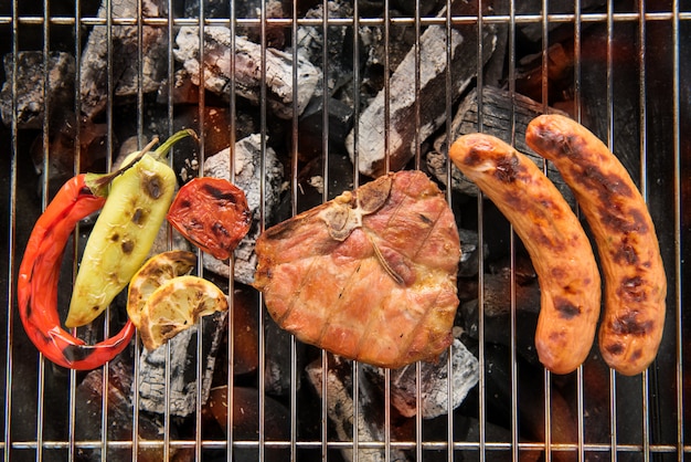 Foto costeleta de porco e legumes com salsicha em uma churrasqueira em chamas.