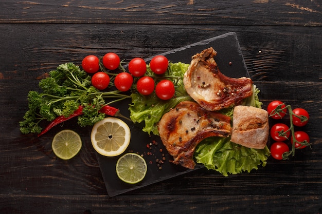 Costeleta de porco frita em um prato preto com especiarias, ervas e tomates.