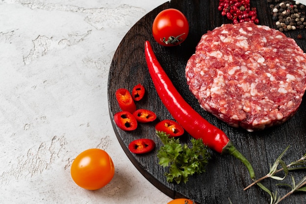 Costeleta fresca e crua feita em casa com especiarias e tomates na mesa, close-up