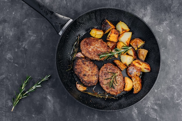 Costeletas de carne com batata frita e alecrim em uma frigideira sobre uma mesa preta