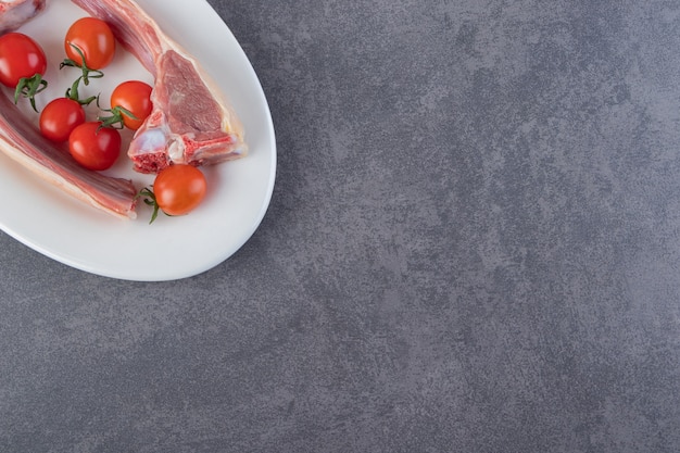 Costeletas de carne crua com tomate cereja na mesa de pedra.