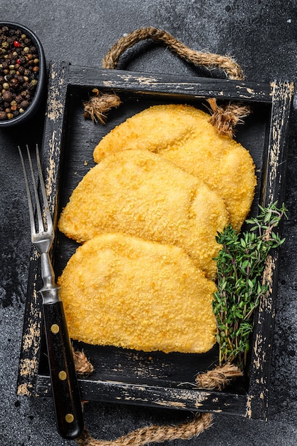 Costeletas de carne crua de cordon bleu em uma bandeja de madeira com ervas.