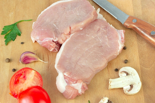 Costeletas de carne de porco crua com alho tomate especiarias pimenta champignon na tábua redonda com faca de carne